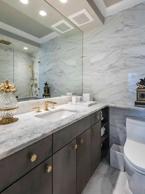 A marble bathroom vanity with a dark cabinet on brass knobs, a brass faucet and a wide mirror