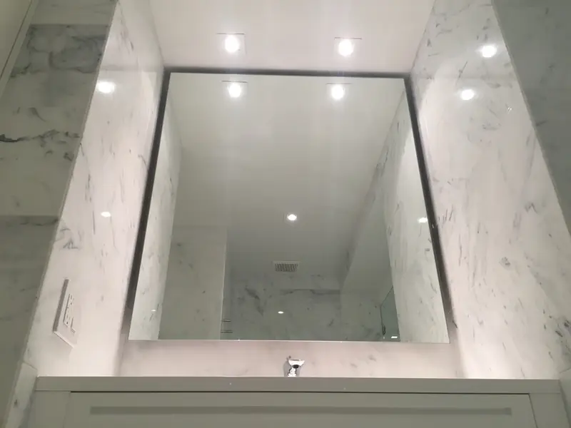 A lit mirror recessed into a white marble bathroom wall, seen from below