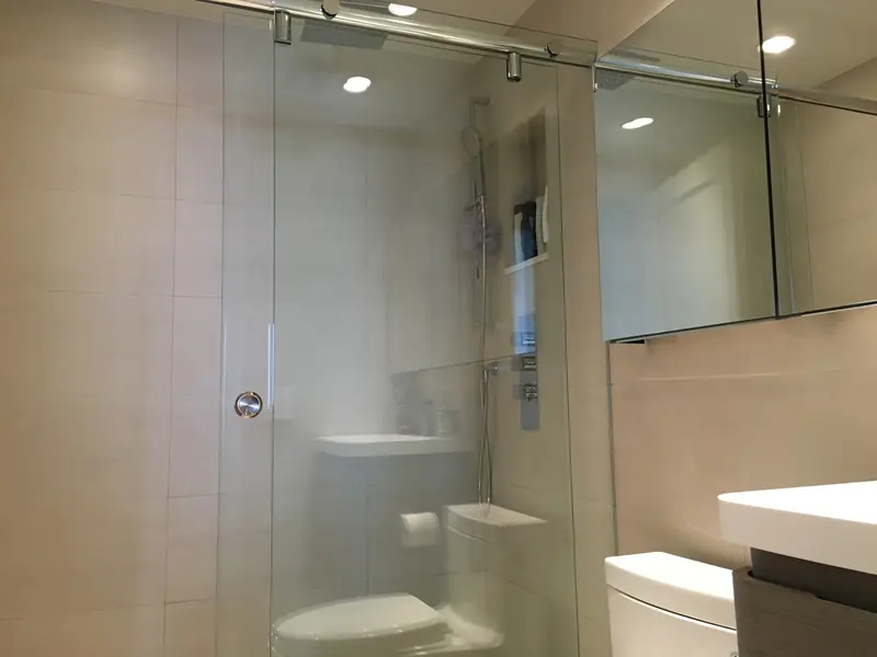 A bathroom with a frameless sliding glass shower door, large beige wall tile and a wide mirror