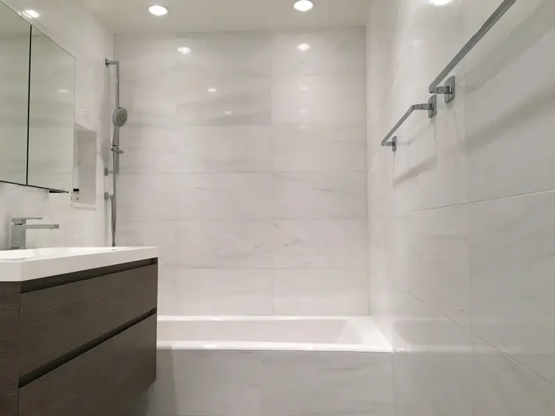 A bathroom tiled in white stone with a soaking tub, a floating wood-grain vanity and a mirrored cabinet