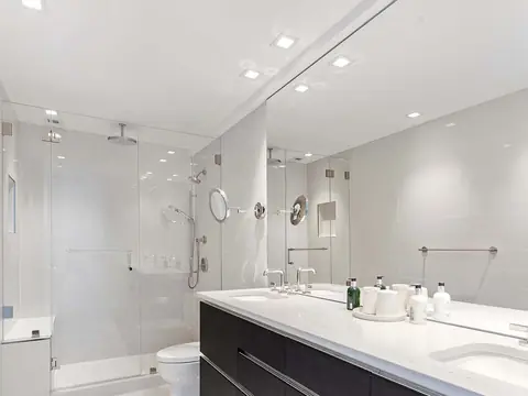 A white bathroom with a long dark double vanity under a white top, a wall-width mirror and a frameless glass shower