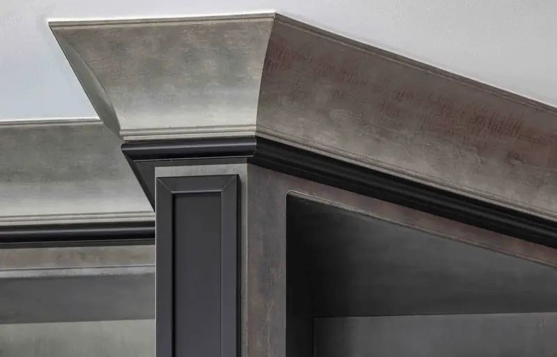 The corner of a grey stained built-in seen from below, showing its crown molding and dark edge bands
