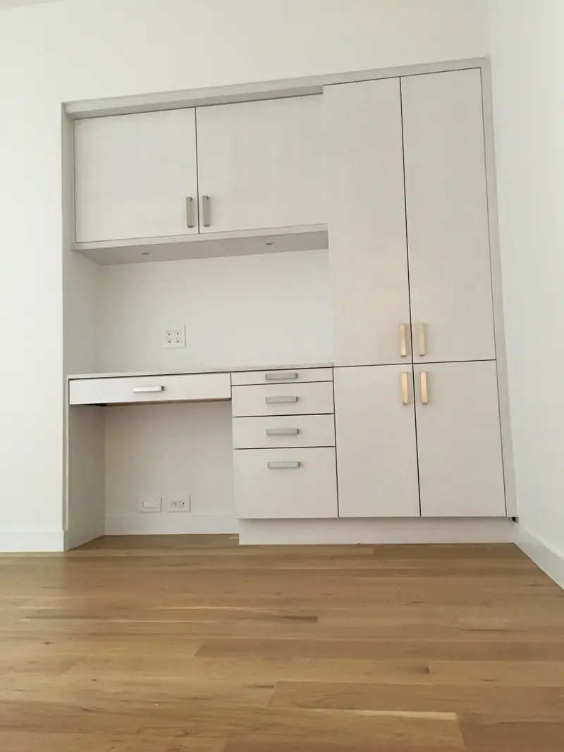 A built-in wall of pale wood-grain cabinets with a desk recess, drawers and tall cupboards on an oak floor