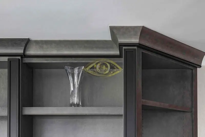 An open shelf of a grey stained built-in with a glass vase, under a stepped crown molding