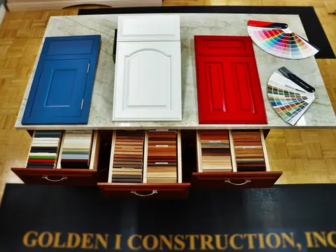 Cabinet door samples in blue, white and red on a stone slab, with paint colour fans and drawers of wood and laminate samples