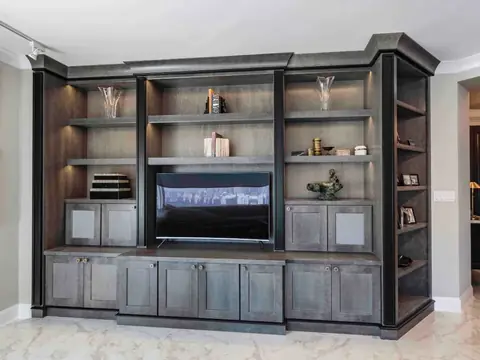 A grey stained built-in entertainment unit with a television, lit shelves, panelled base cabinets and a crown along the top