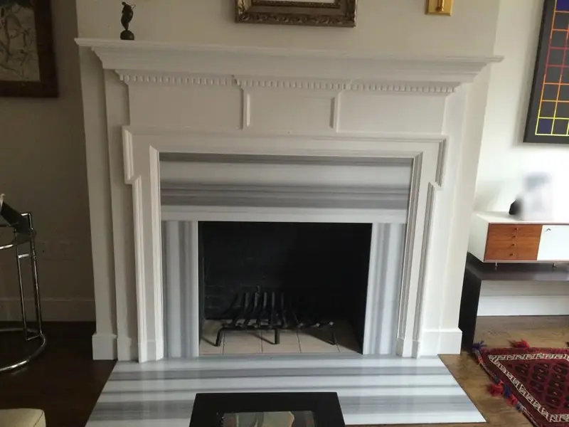 A fireplace with a white classical mantel and a grey and white striped marble surround and hearth