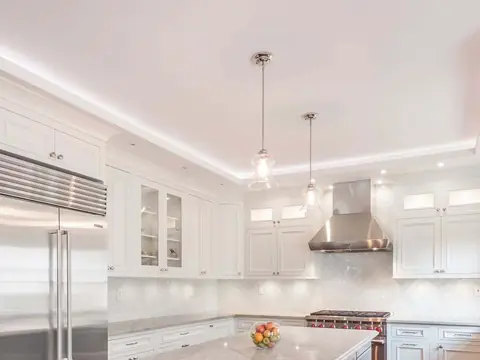 A kitchen with white cabinets to the ceiling, a steel refrigerator, a steel hood and two glass pendants
