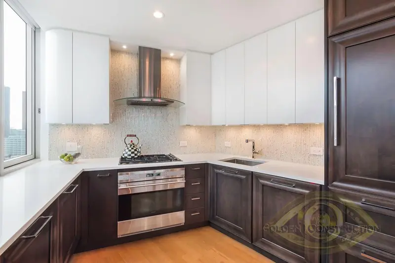 A kitchen with dark wood base cabinets, white wall cabinets, a gas cooktop under a steel and glass hood and a mosaic backsplash
