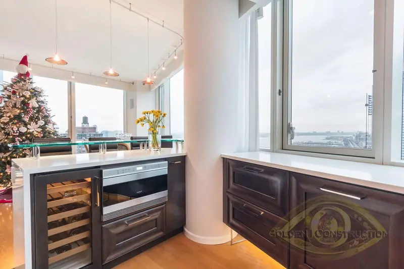 A kitchen peninsula with a wine refrigerator and a steel drawer oven under a raised glass counter, with windows onto a river