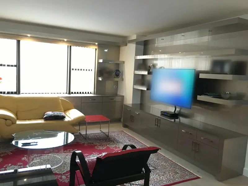 A living room with a long grey built-in wall of base cabinets and floating shelves around a television, with a yellow sofa