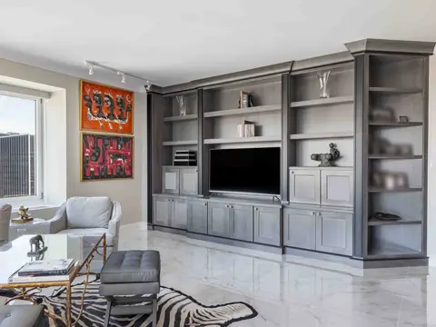A living room with a grey stained built-in media wall around a television, a white marble floor and a zebra hide rug