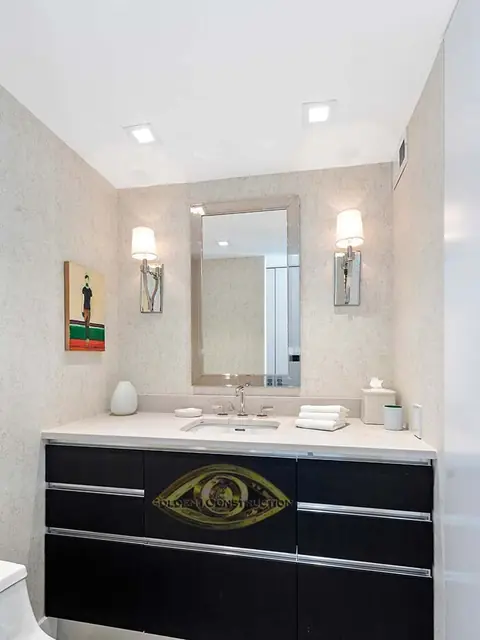 A powder room with a black vanity under a white top, a framed mirror between two sconces and textured wall covering