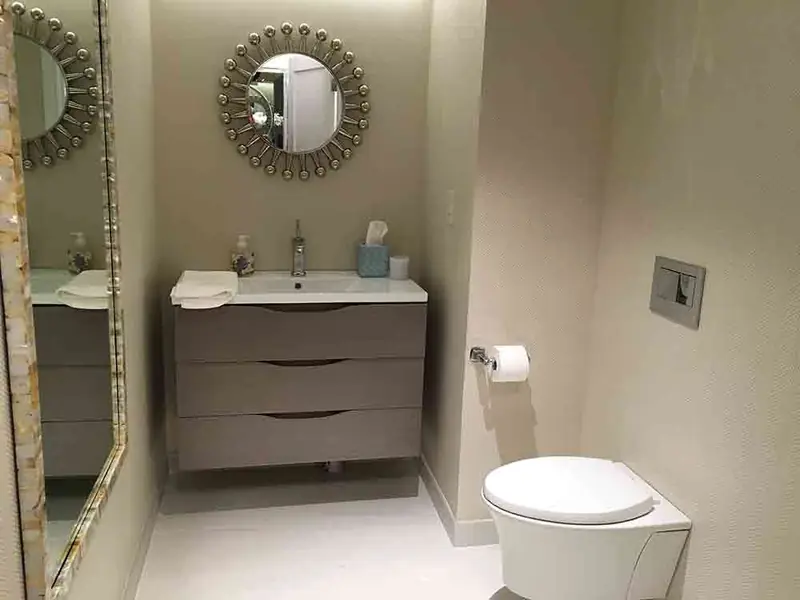 A powder room with a floating grey vanity with three drawers, a round sunburst mirror and a wall-hung toilet
