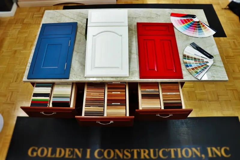 Cabinet door samples in blue, white and red on a stone slab, with paint colour fans and drawers of wood and laminate samples