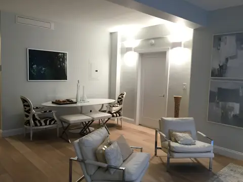 A sitting and dining corner with an oval table, zebra-print chairs, two white armchairs and two wall sconces beside a door